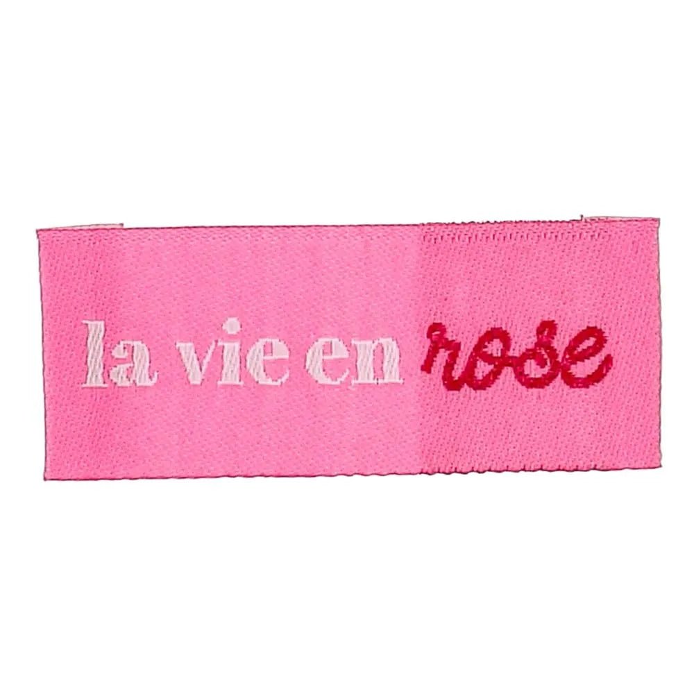Pilt Bochini riiete sisseõmmeldavatest siltidest „La vie en rose” – vaata elu läbi roosade prillide – 2 × 5 cm, 4 tk – saadaval veebis Šarlotes audumi