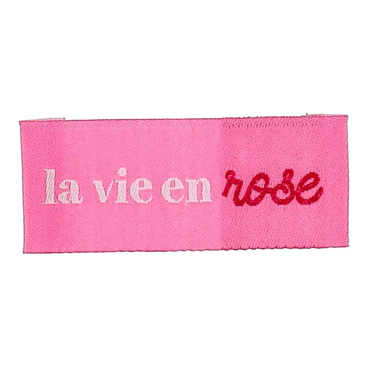 Pilt Bochini riiete sisseõmmeldavatest siltidest „La vie en rose” – vaata elu läbi roosade prillide – 2 × 5 cm, 4 tk – saadaval veebis Šarlotes audumi